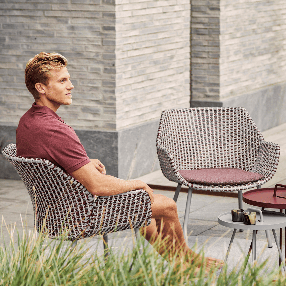 Boxhill's Vibe light grey / maroon outdoor armchair with a man sitting on it with grey and maroon round outdoor side table