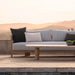 Patio with wooden framed 3-seat outdoor sofa with light gray cushions, pillows, and wooden coffee table overlooking distant hills.