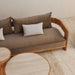 Wooden outdoor 3-seater sofa with brown cushions, white pillows, and two beige round textured coffee tables on tiled patio.
