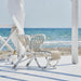 White rattan outdoor lounge chair with a sculptural woven frame on a seaside patio.
