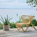 Natural rattan outdoor lounge chair with a curved woven frame on a seaside deck.