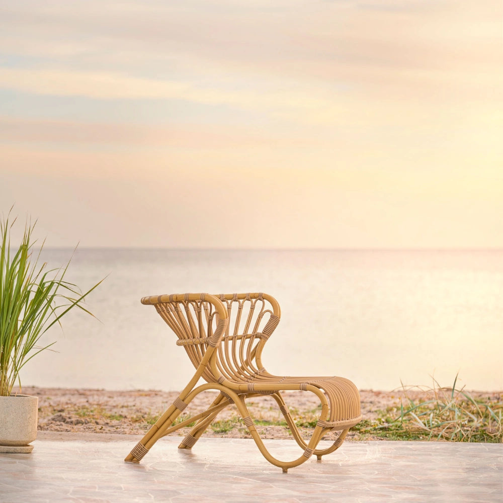 Natural rattan outdoor lounge chair with a curved woven frame on a seaside patio.