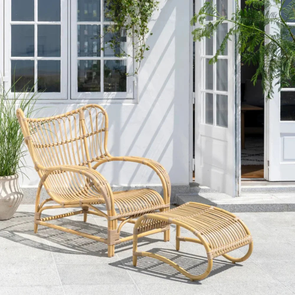 Natural rattan outdoor lounge chair with a matching footstool on a sunny patio.