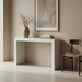 Minimalist beige living room with a white concrete console table, a rustic vase with branches, stacked books, and a wooden chair
