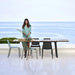 Boxhill's Copenhagen Coastal Dining Table lifestyle image at seafront with Copenhagen Dining Chair and  a woman standing beside