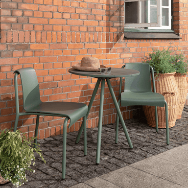 2 green armless outdoor dining chairs and green round outdoor coffee table set on a patio against orange brick wall