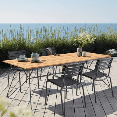 A Bamboo lamellas rectangular outdoor dining table 4 dark gray outdoor dining chairs set on a wooden deck surrounded by tall grass