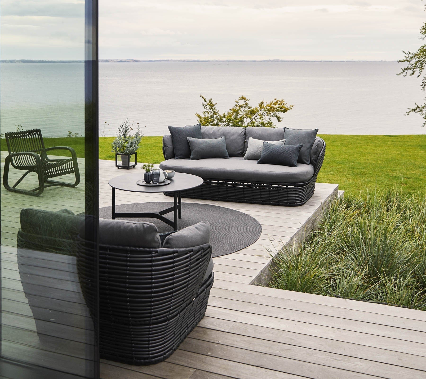 Boxhill's Basket 2-Seater Outdoor Sofa Graphite lifestyle image on wooden platform at seafront