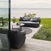 Boxhill's Basket 2-Seater Outdoor Sofa Graphite lifestyle image on wooden platform at seafront