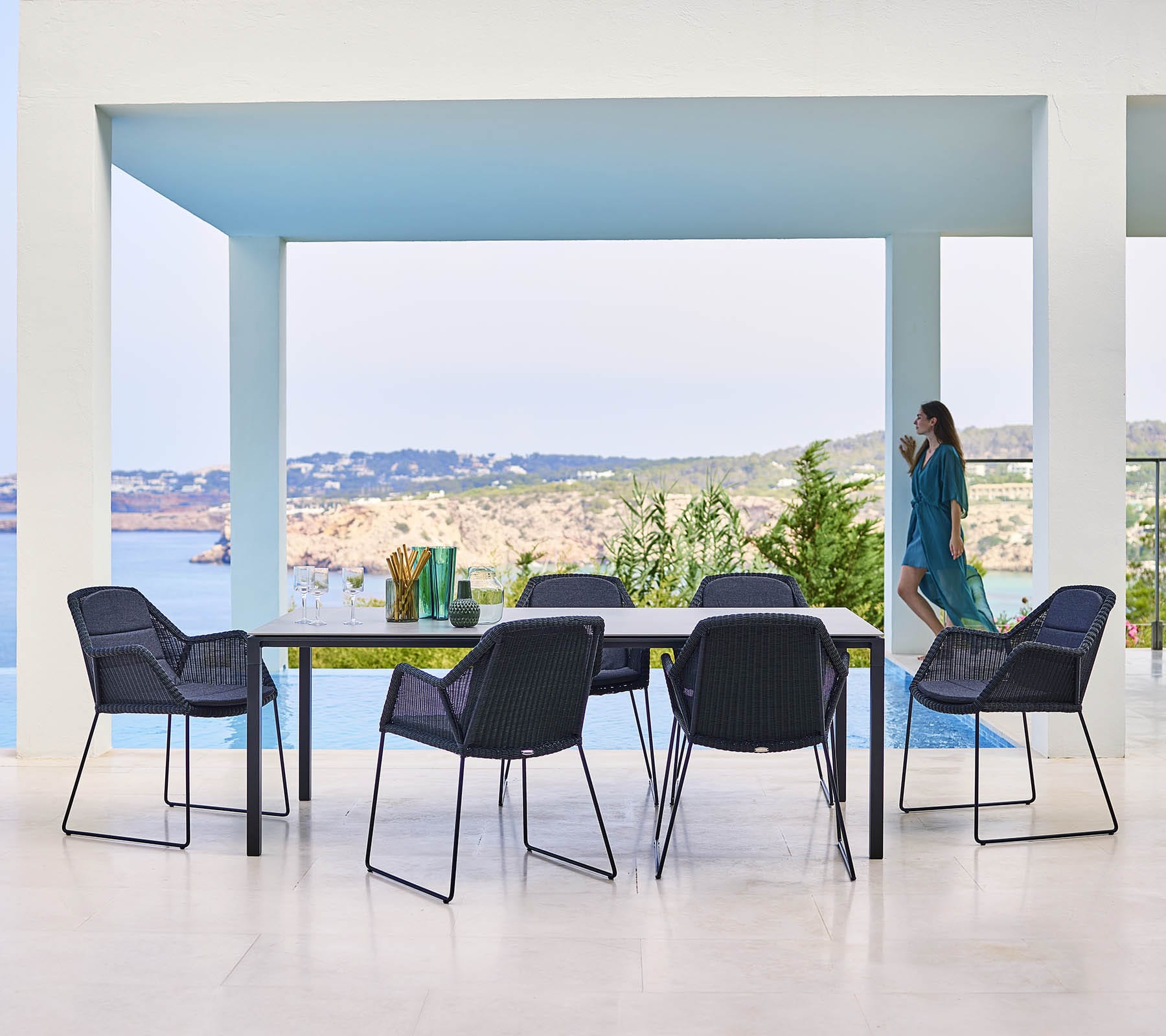 Boxhill's Breeze Dining Weave Chair Black lifestyle image with dining table beside the pool with woman standing