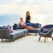 Boxhill's Moments Outdoor Corner Module lifestyle image at seafront with Moments 2-Seater Right Module Sofa and 2 Women, 1 is sitting and 1 is standing