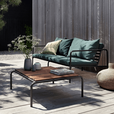 A wooden outdoor lounge table with black metal frame and a dark green outdoor lounge chair set on a wooden deck patio