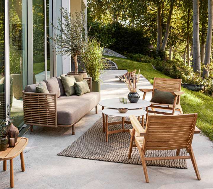 Boxhill's Sense light brown 3-seater outdoor sofa with 2 white round tables, 2 teak chairs and teak side table placed in patio