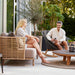 boxhill's Sense light brown 3-seater outdoor sofa with dark grey outdoor lounge chair with man and a woman sitting having a chat