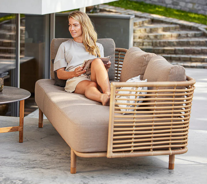 Boxhill's Sense light brown 3-seater outdoor sofa with a woman sitting on it reading a magazine