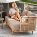 Boxhill's Sense light brown 3-seater outdoor sofa with a woman sitting on it reading a magazine