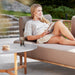 Boxhill's Sense light brown 3-seater outdoor sofa with a woman sitting on it and light grey outdoor round table with teak base