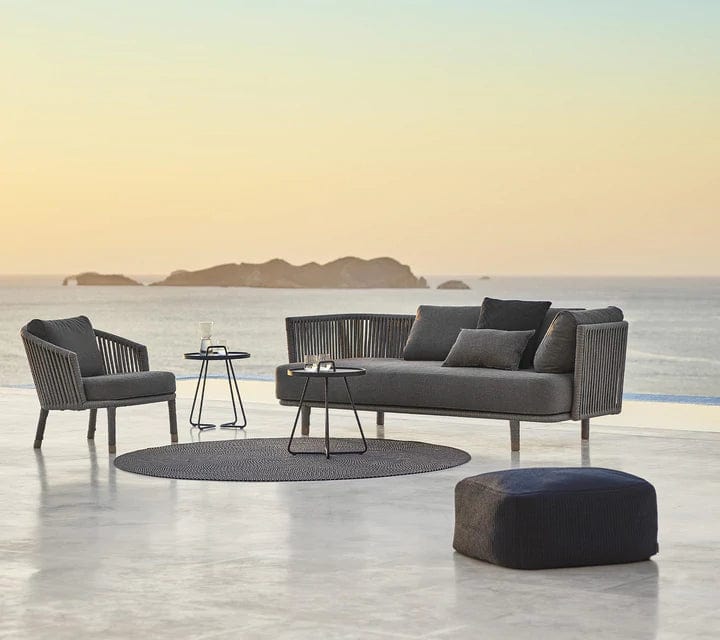 Boxhill's Moments 3-Seater Sofa lifestyle image with Moments Outdoor Lounge Chair, 2 round table and fabric footstool at seafront
