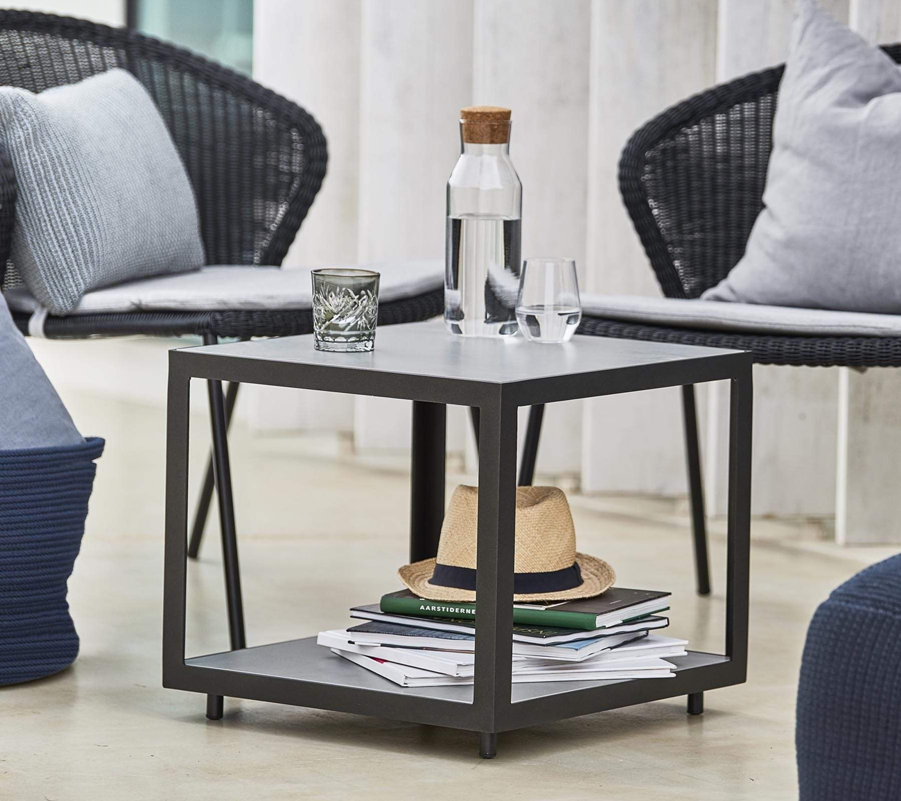 Boxhill's LEVEL Square Coffee Table Lava Grey lifestyle image with 2 glasses of water and bottle container on top, and a hat and books under