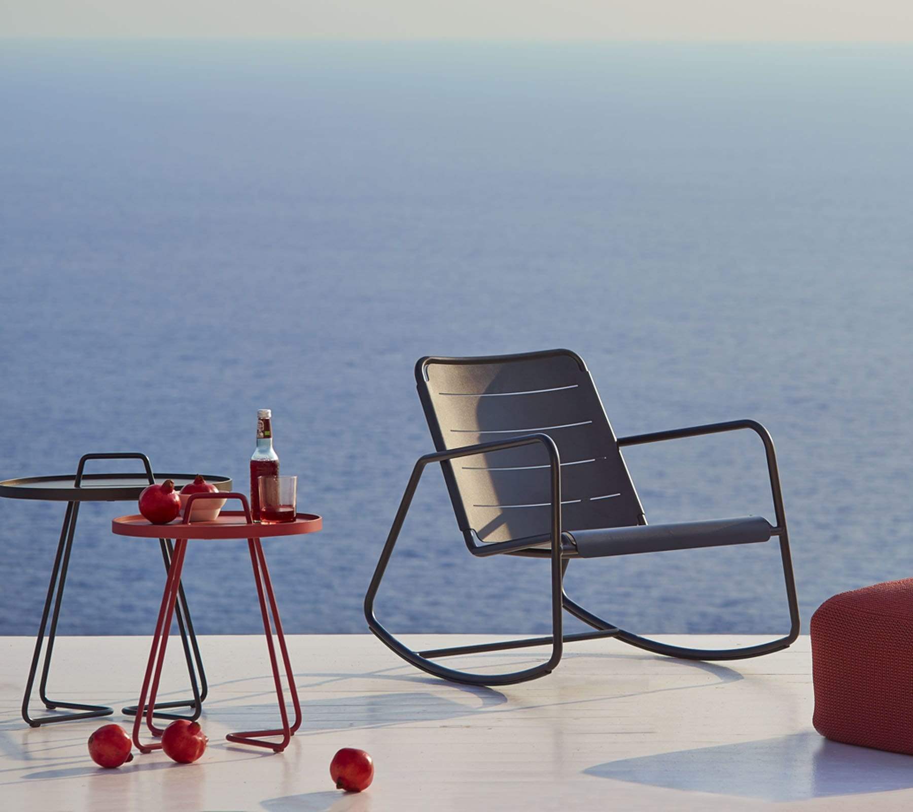 Boxhill's Copenhagen Rocking Chair lifestyle image with side tables and red footstool at sea front