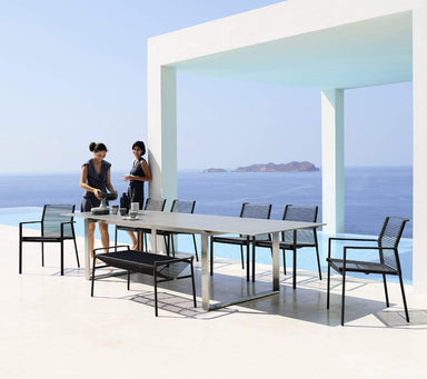 Boxhill's Edge Stackable Outdoor Armchair lifestyle image with long dining table and 2 women standing beside the pool