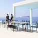Boxhill's Edge Stackable Outdoor Armchair lifestyle image with long dining table and 2 women standing beside the pool