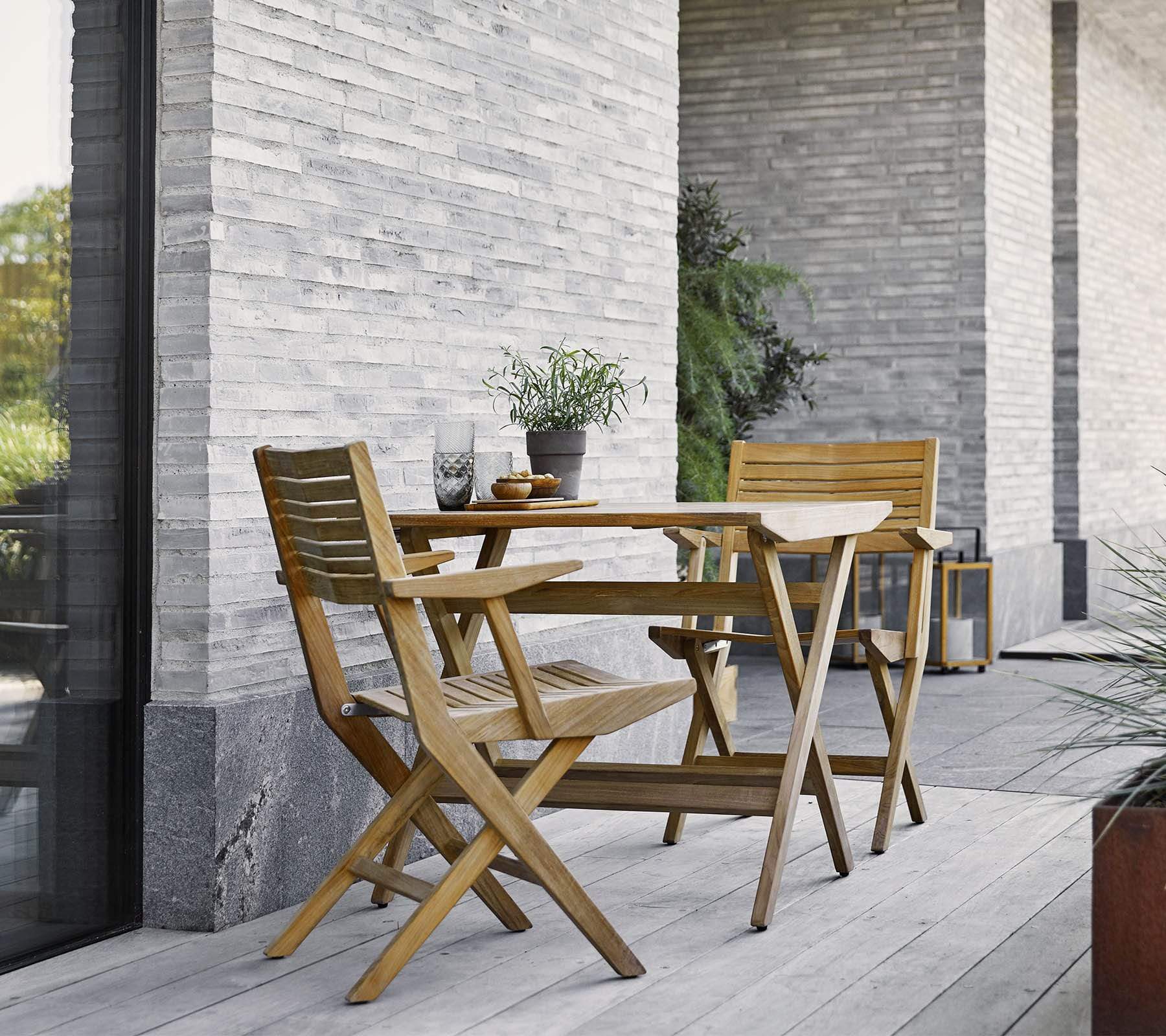 Boxhill's Flip Folding Outdoor Teak Dining Armchair lifestyle image with Flip Folding Outdoor Teak Dining Table at patio beside the wall