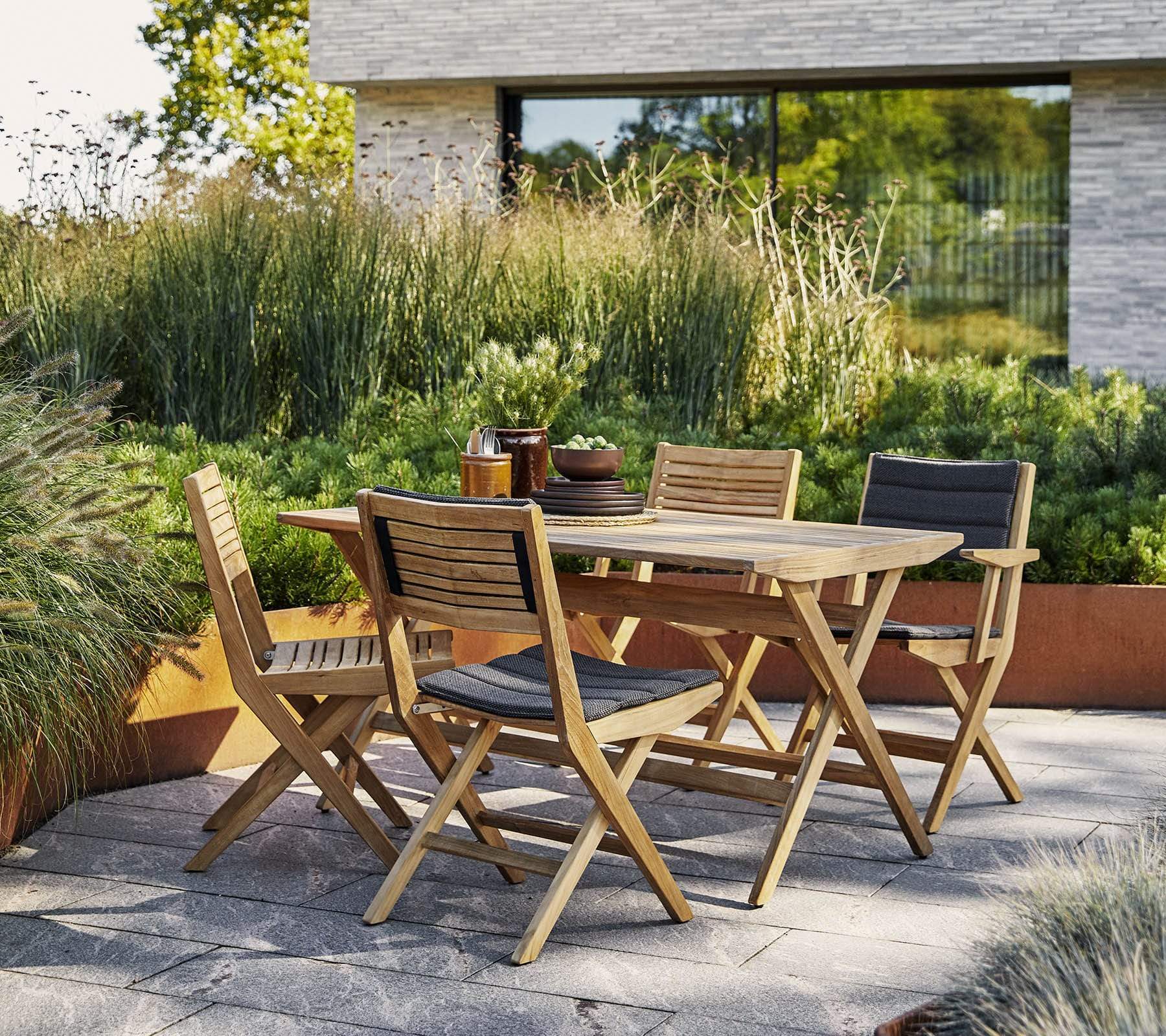 Boxhill's Flip Folding Outdoor Teak Dining Armchair lifestyle image with Flip Folding Outdoor Teak Dining Table beside plants at patio