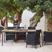 Boxhill's Hampsted Outdoor Dining Armchair lifestyle image with Core Garden Dining Table beside the tree and 2 women standing at the side
