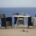 Boxhill's Hampsted Outdoor Dining Armchair lifestyle image with round table on wooden platform at seafront