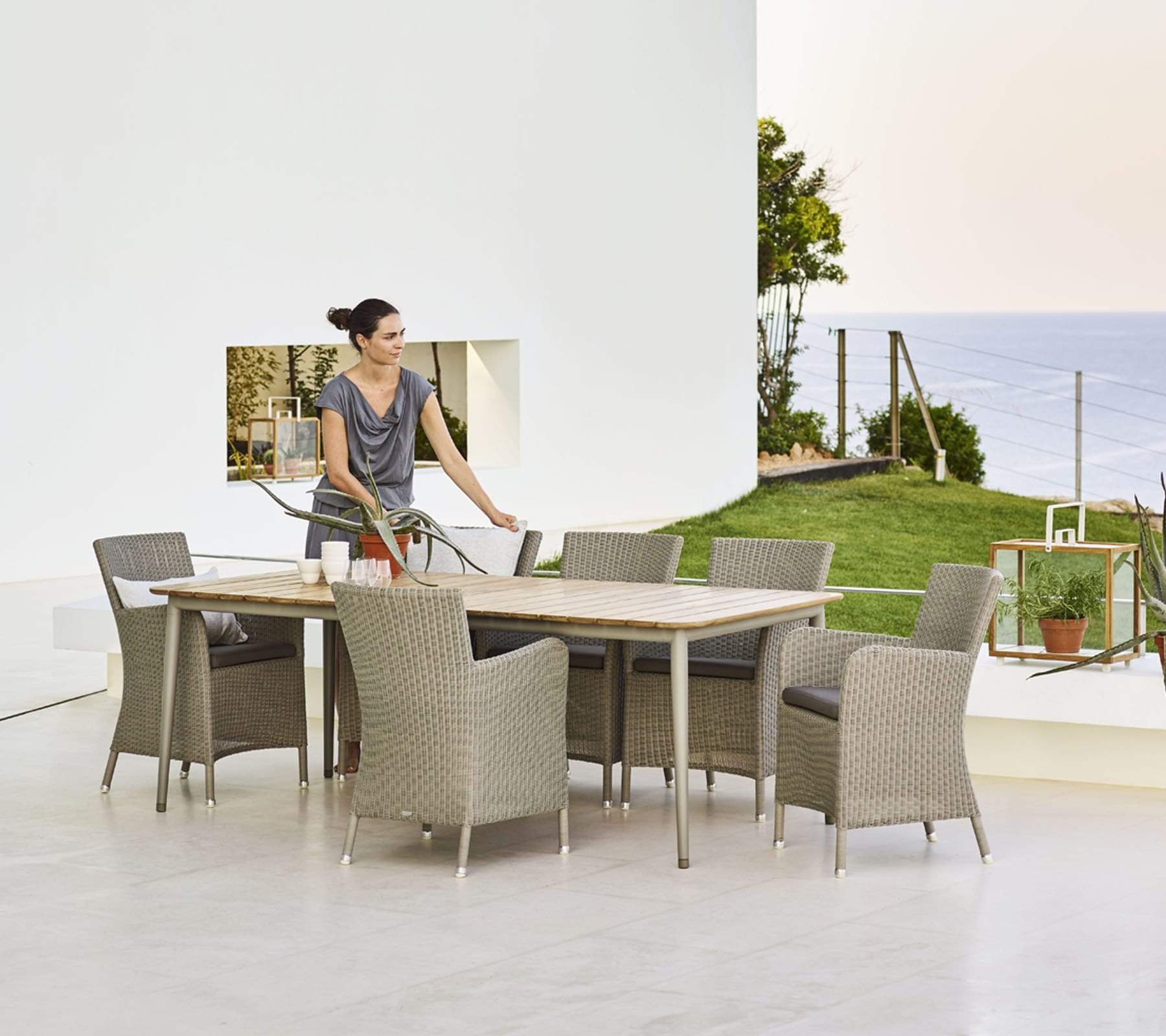 Boxhill's Hampsted Outdoor Dining Armchair lifestyle image with Core Garden Dining Table with a woman standing at the side, at patio