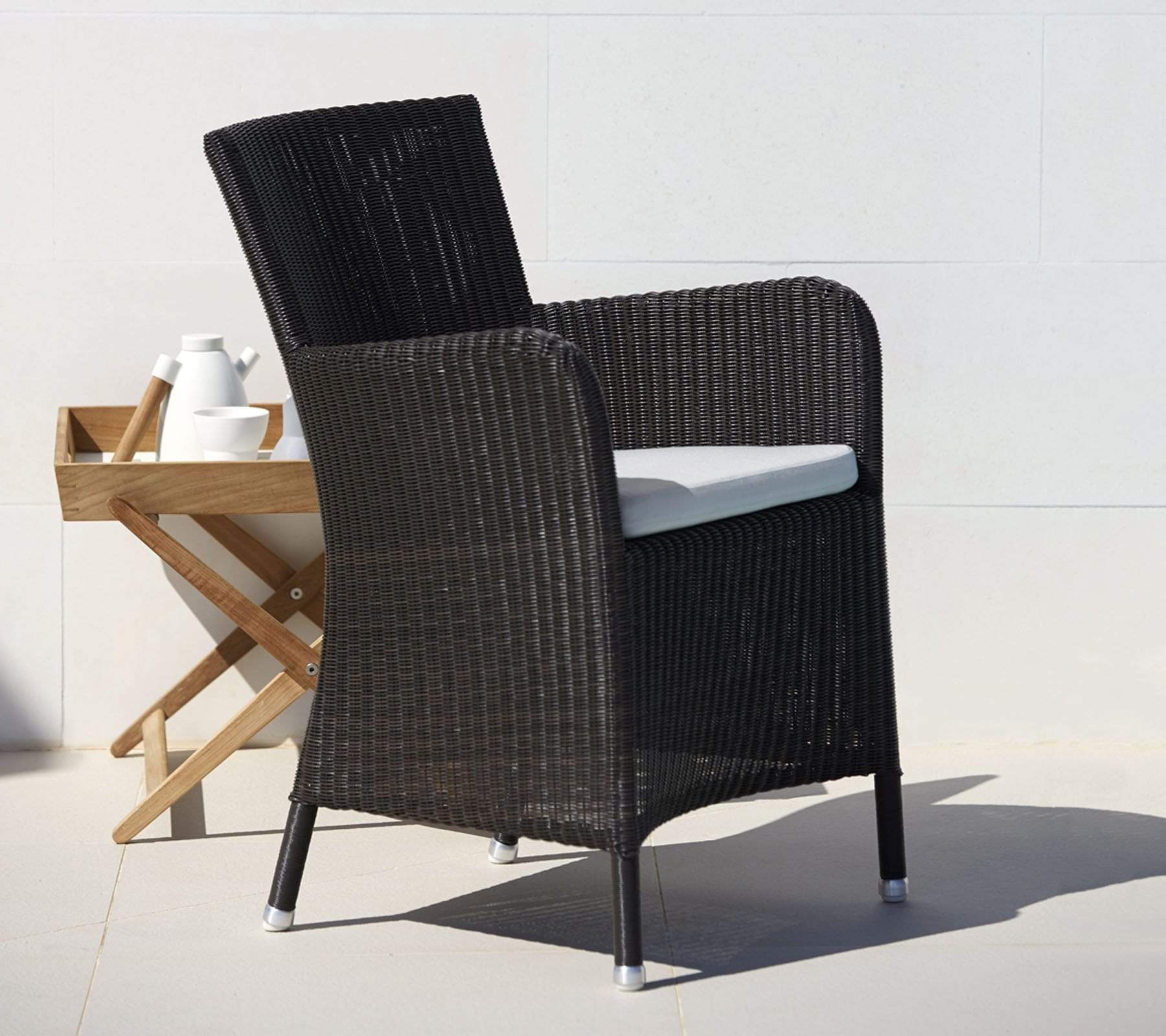Boxhill's Hampsted Outdoor Dining Armchair Black Weave with White Cushion lifestyle image with teak side table