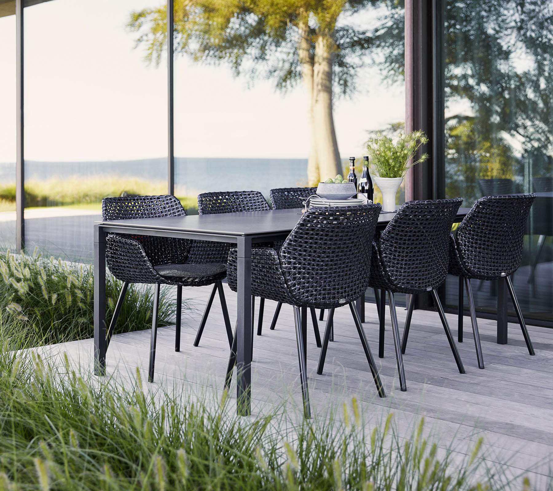 Boxhill's Vibe black outdoor armchair with dark grey outdoor dining table placed on wooden platform beside glass wall