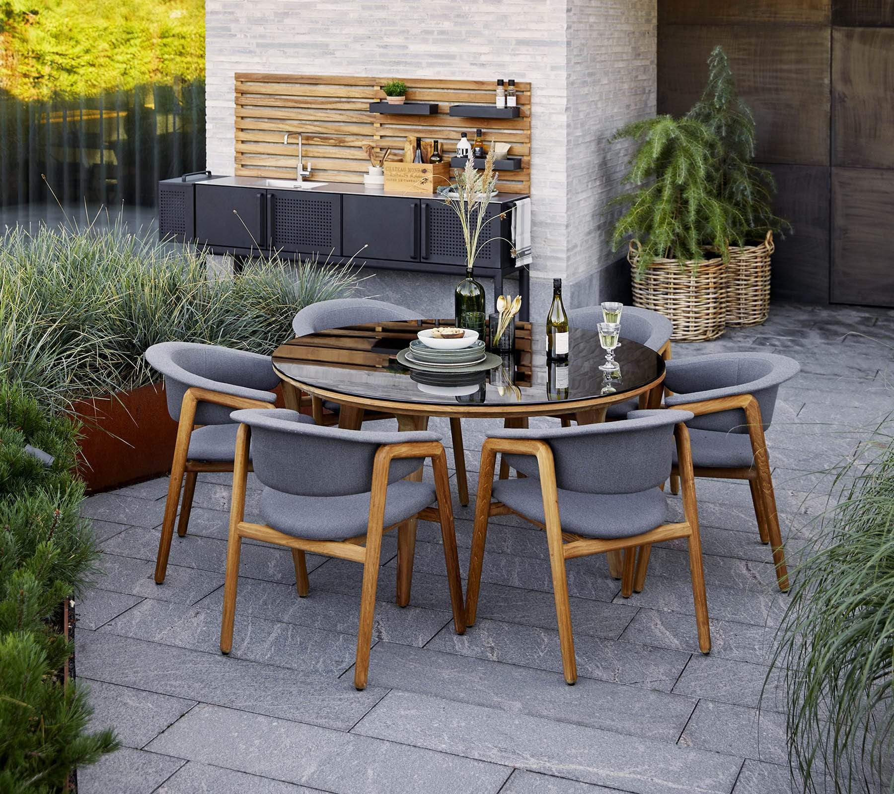 Boxhill's Aspect Teak Round Dining Table Clear Glass | Smokey Black lifestyle image with dining chairs at the garden