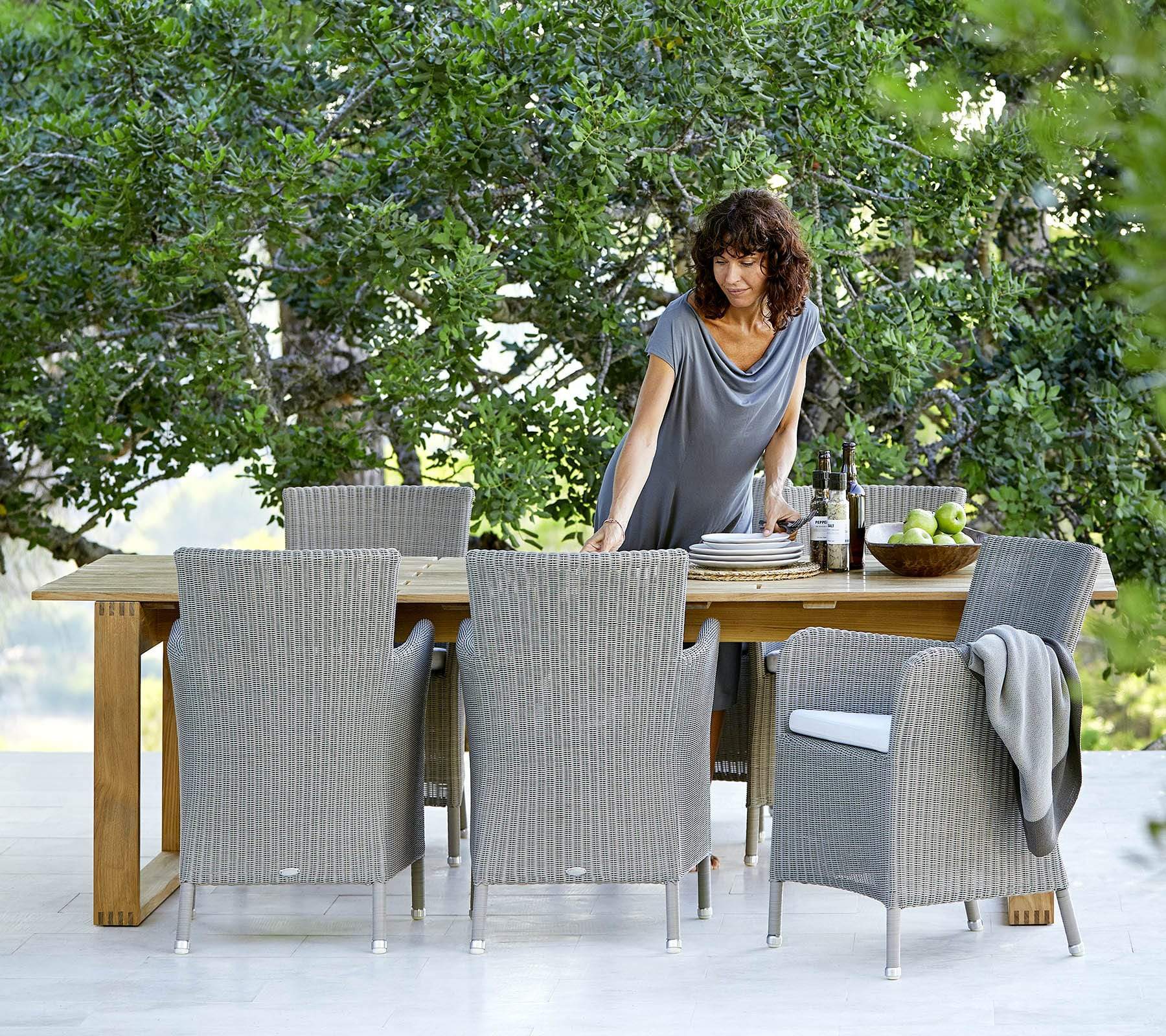 Boxhill's Endless Outdoor Rectangular Dining Table lifestyle image with dining chairs and a woman standing at the side arranging the plates