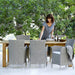 Boxhill's Endless Outdoor Rectangular Dining Table lifestyle image with dining chairs and a woman standing at the side arranging the plates