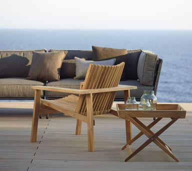 Boxhill's Amaze Stackable Lounge Teak Chair lifestyle image on wooden platform at the beach side 