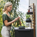 Boxhill's Drop Outdoor Kitchen Module Single with 2 Shelves and Teak Wall lifestyle image with a woman mixing vegetables in a bowl 