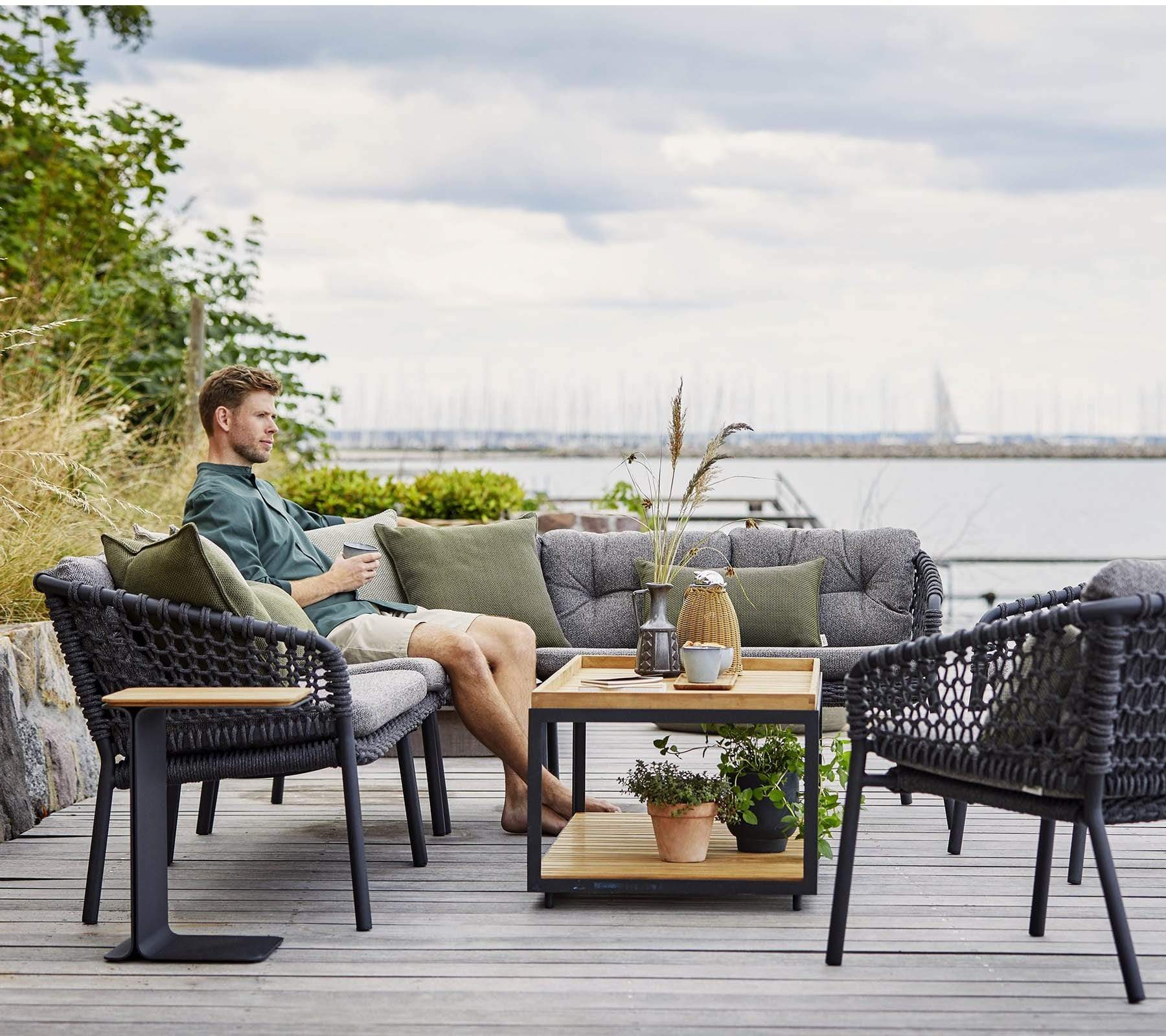 Boxhill's Ocean 2-Seater Outdoor Left Module Sofa lifestyle image with other Ocean Module Sofa Collection,  Level Coffee Table with Teak Top, and a man sitting down holding a cup of coffee